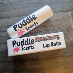 Two strawberry lip balms from Puddle Scents on a wooden surface